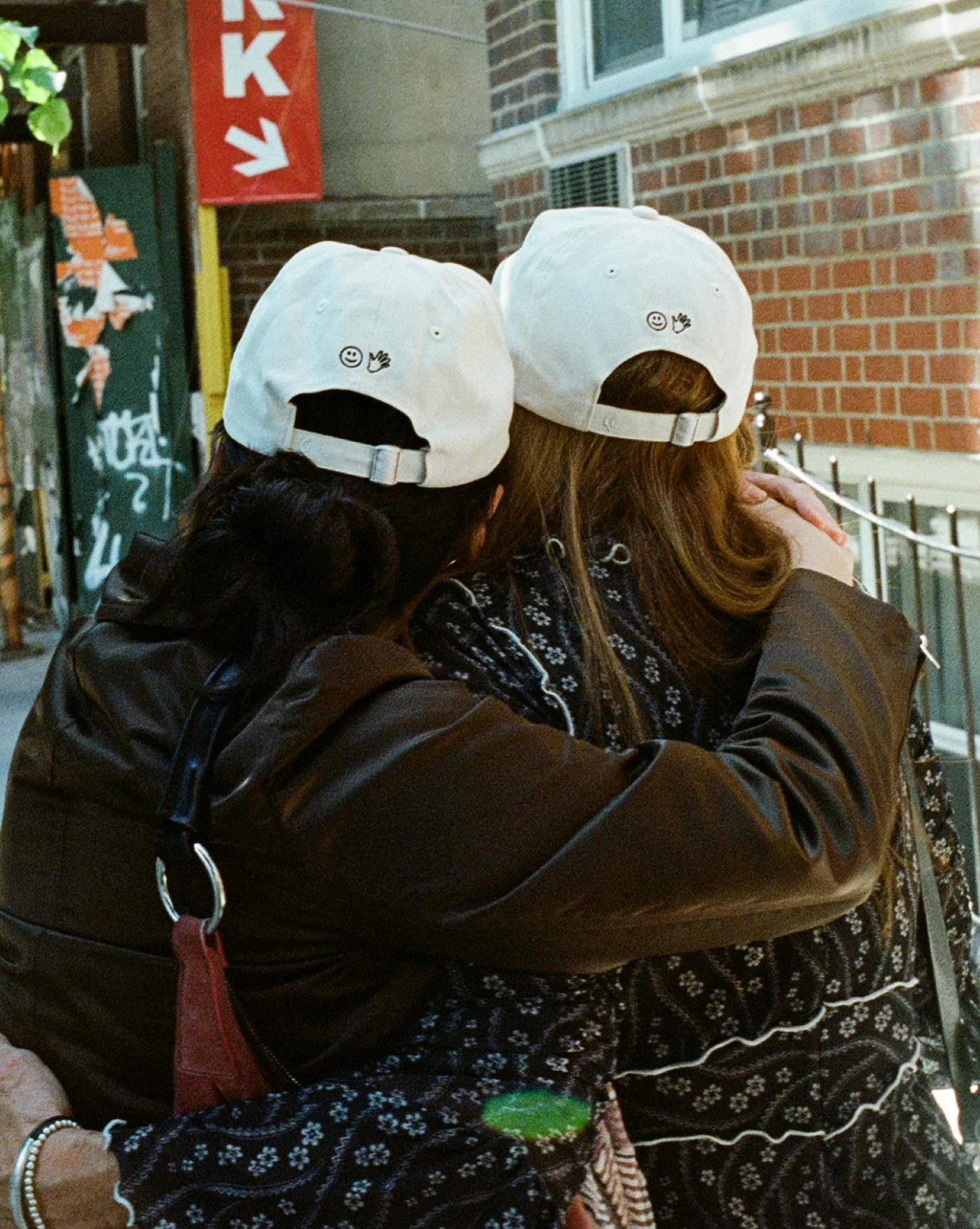 two friends wearing you look good caps embracing